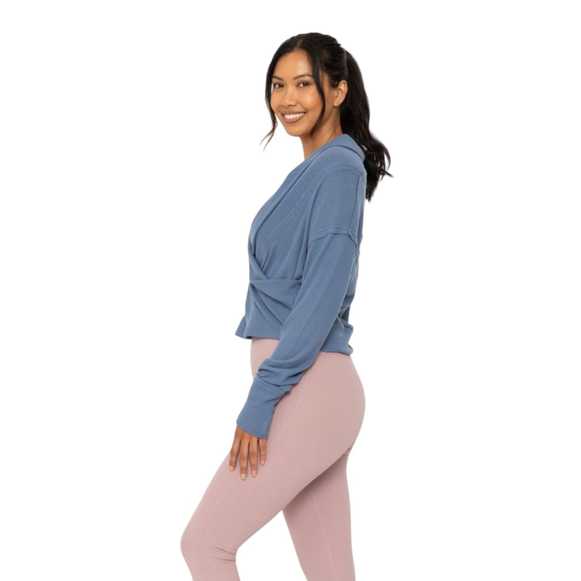 Stylish woman in a blue ribbed wrap top paired with pink leggings, showcasing activewear comfort and chic design.