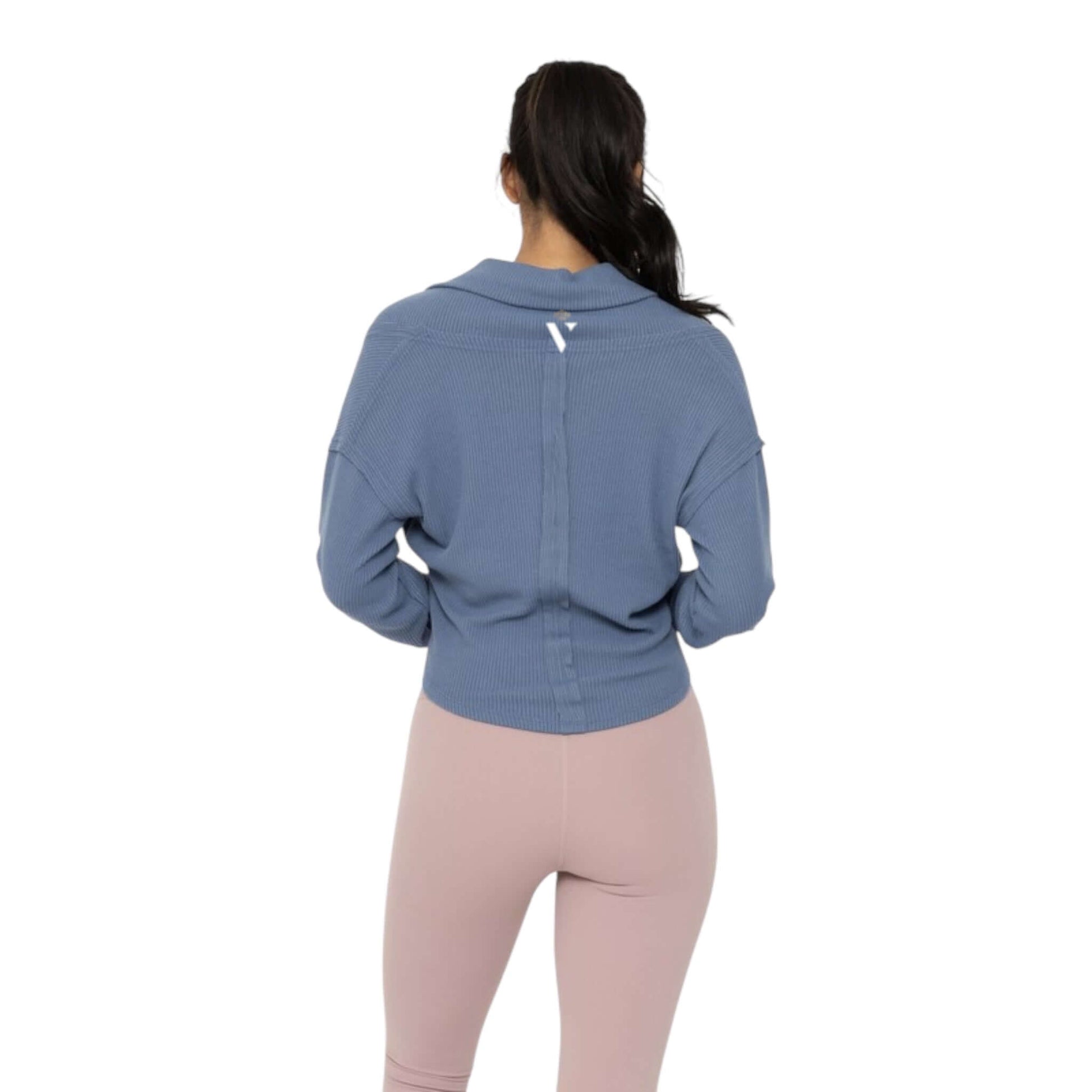 Back view of a woman in a blue ribbed wrap top, paired with light pink leggings, showcasing a stylish activewear look.