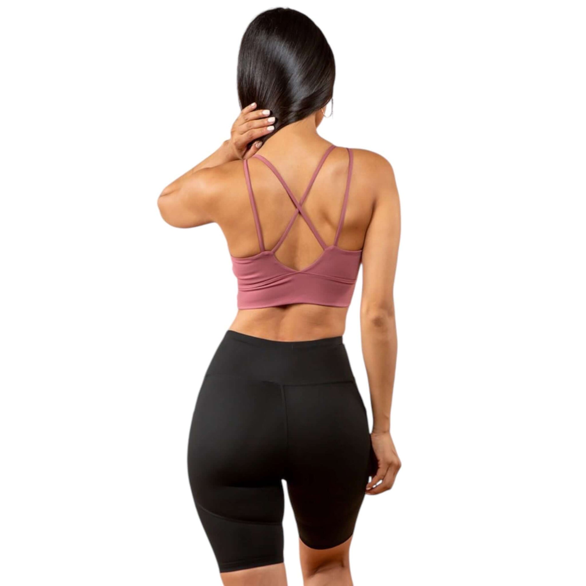 Back view of a woman wearing a pink peekaboo sports bra with cross back design and black shorts, showcasing activewear style.