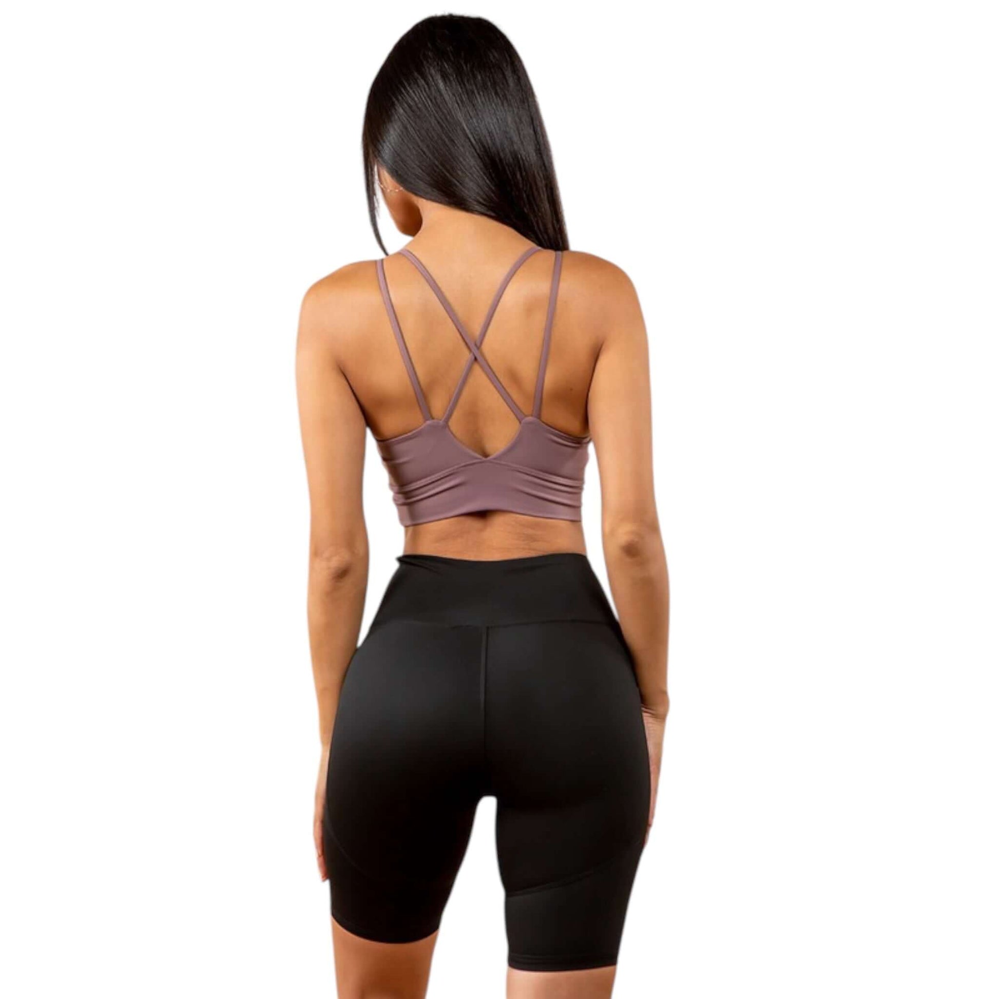 Model wearing a purple peekaboo sports bra with cross back design and black shorts, showcasing stylish activewear.